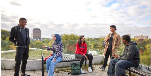 A group of students sitting on an outdoor terrace overlooking the Keele campus