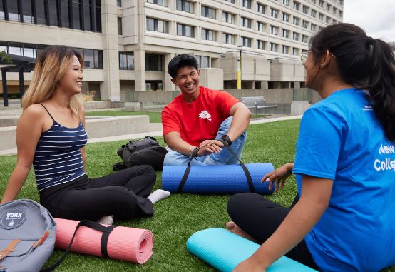three students sitting on the grass with yoga mats